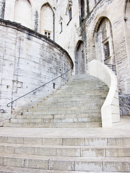 colour photograph, portrait layout, looking at a large set of stone steps curving round, with a high wall on one side and stone walls with windows in the background